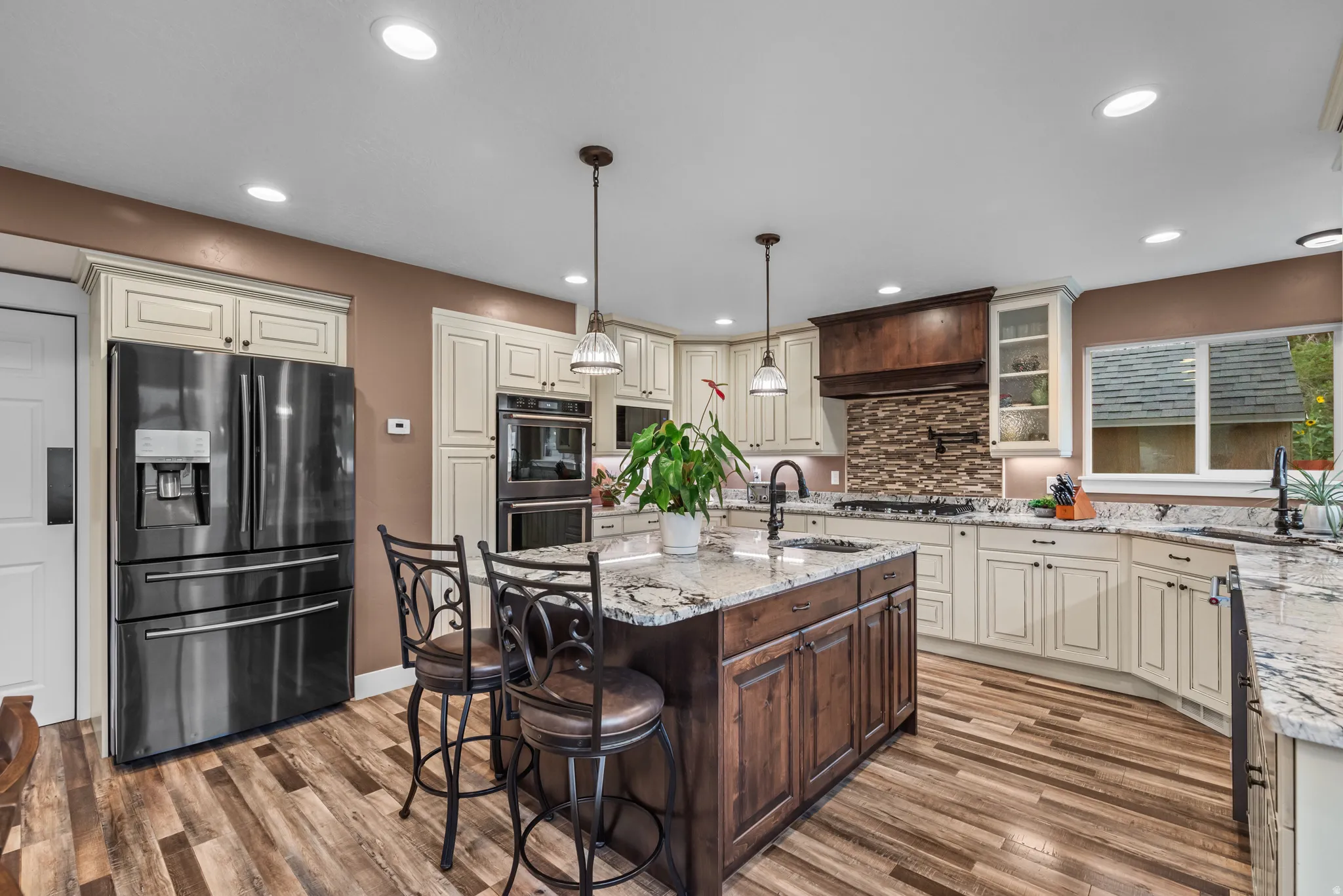 Gourmet kitchen featuring a wood-finish floor, two-tone cabinetry, stone countertops, a tiled backsplash, and stainless steel appliances