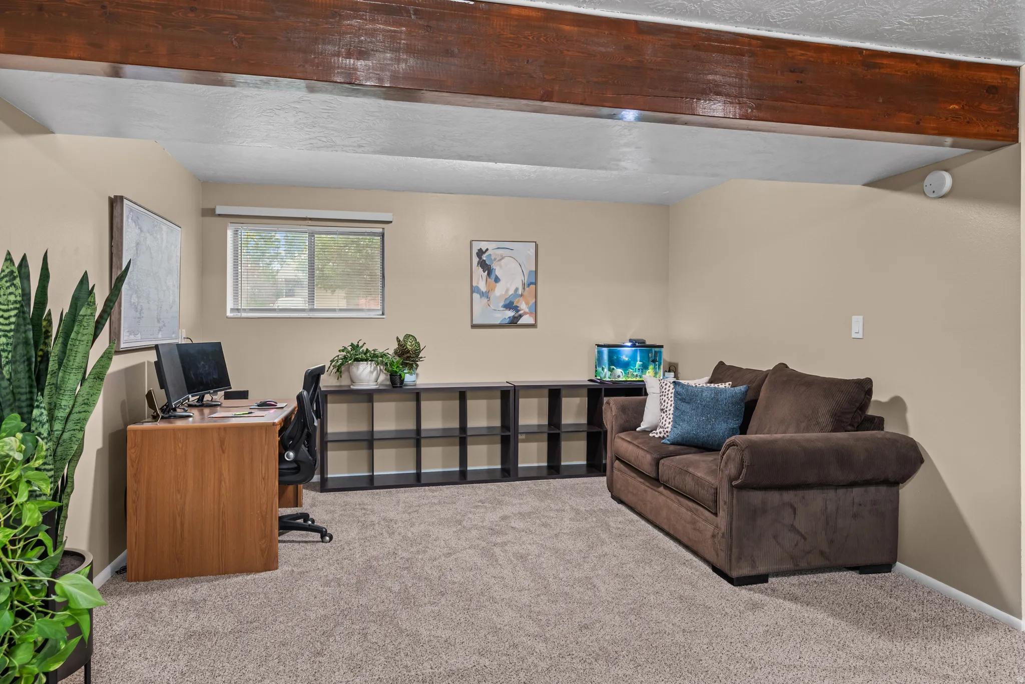Carpeted room featuring exposed wood beams, light beige walls, a window with a blind, and a built-in shelving unit