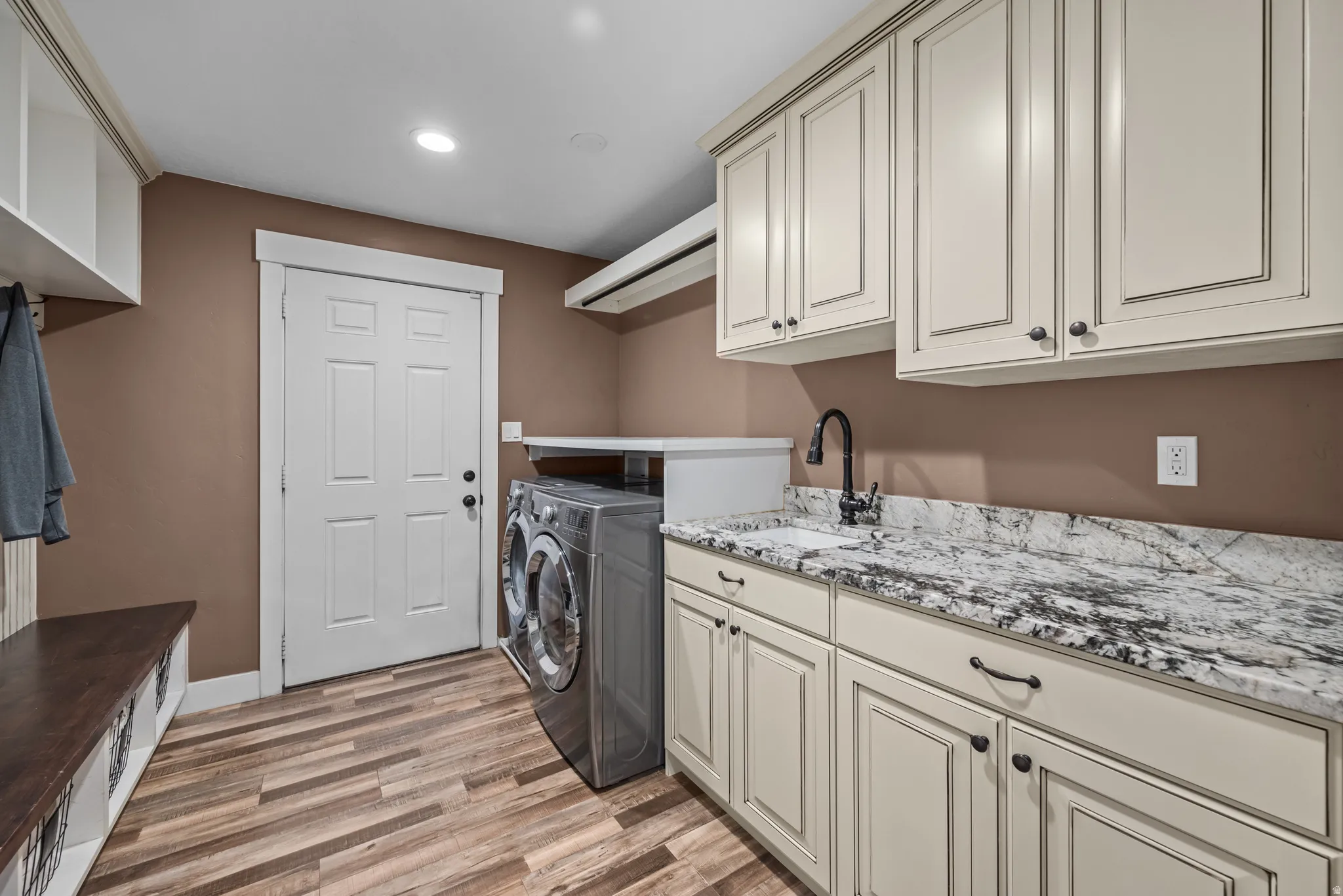 Dedicated laundry area featuring wood-finish flooring, light-toned cabinetry, and a countertop with integrated sink