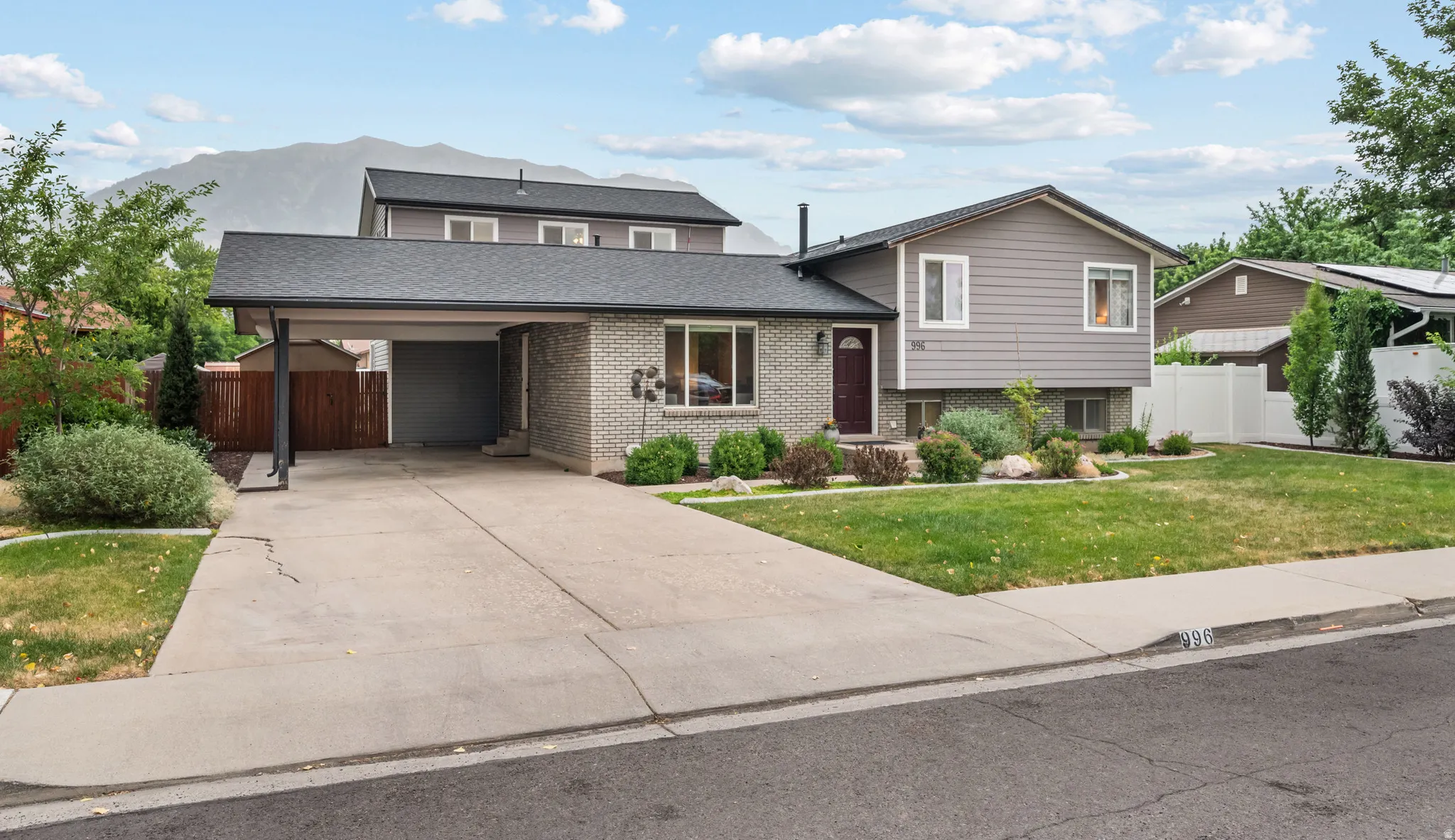 Split-level residence featuring a carport, a two-tone exterior with gray brick and siding, a red entry door, a landscaped front yard, and a concrete driveway