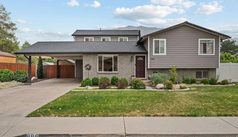 Split-level residence featuring a carport, a two-tone exterior with gray brick and siding, a dark entry door, and a landscaped front yard