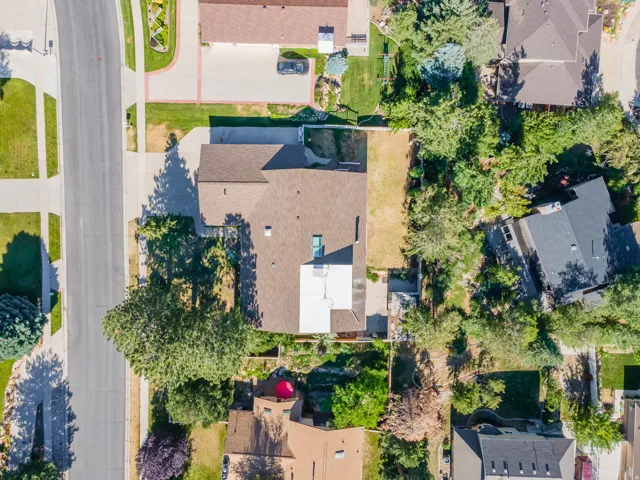 Property featuring a shingled roof, a paved driveway, and mature landscaping