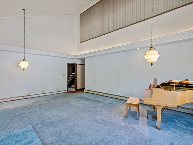 Spacious room featuring vaulted ceilings, decorative crown molding, pendant lighting, textured wall paneling, and baseboard heating