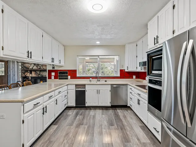 Kitchen featuring white cabinetry, wood-finish flooring, stainless steel appliances, and a red tile backsplash