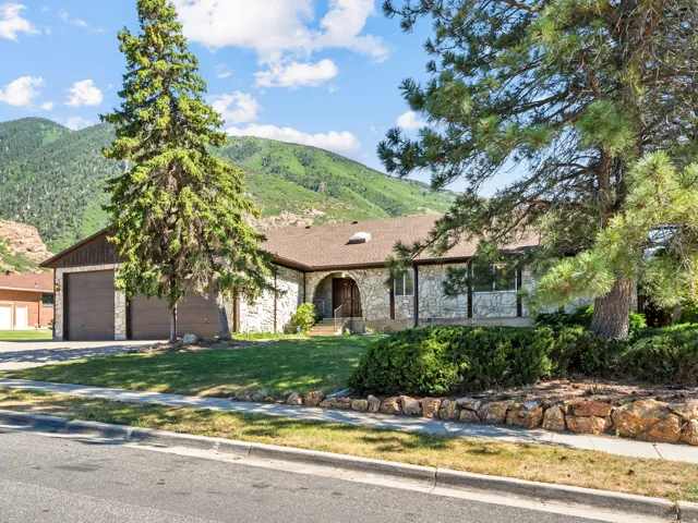Stone exterior residence featuring a two-car garage, mature landscaping, and an arched entry