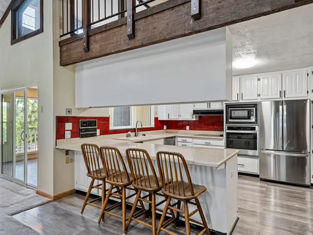 Kitchen featuring white cabinetry, stainless steel appliances, red tile backsplash, and a breakfast bar with solid surface countertops