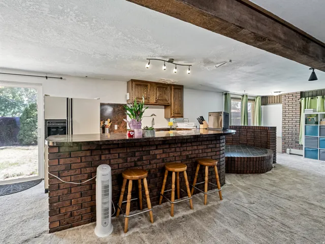 Open-concept space featuring a brick-faced bar with seating, wood-finish cabinetry, and built-in appliances