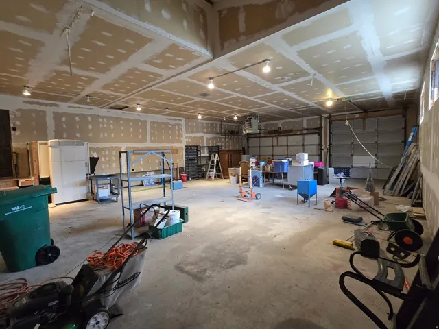 Expansive interior space featuring concrete flooring, unpainted drywall, exposed overhead lighting, and two garage doors