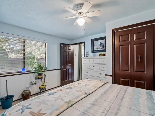 Bedroom featuring a ceiling fan with integrated lighting, a wide window with horizontal blinds, and paneled wainscoting