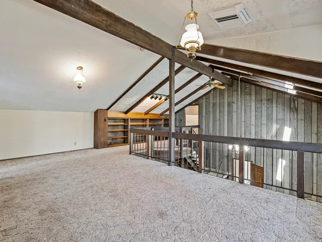Carpeted loft space featuring exposed wood beams and architectural ceiling angles