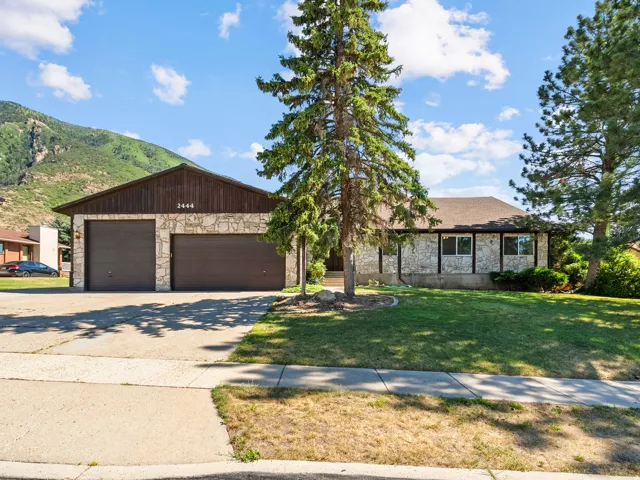 Stone and wood-sided residence featuring a two-car garage with individual doors, a concrete driveway, and a front lawn