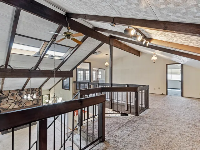 Vaulted ceiling with exposed wood beams, skylights, and a ceiling fan