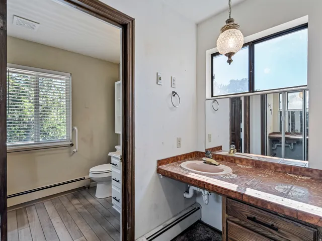 Bathroom featuring a wood-finish vanity with a tile countertop and integrated sink, a large wall-mounted mirror, and a decorative pendant light fixture