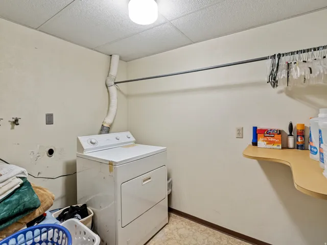 Dedicated laundry area featuring a white dryer, overhead hanging rod, and a wall-mounted utility shelf