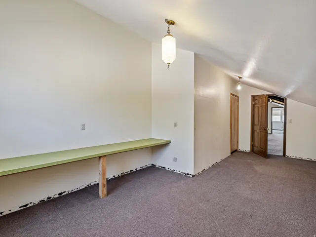 Room featuring sloped ceilings, wall-to-wall carpeting, and a built-in desk surface