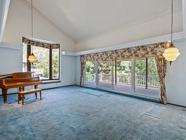 Spacious room featuring vaulted ceilings, a large bay window, and a wall of sliding glass doors opening to an outdoor deck