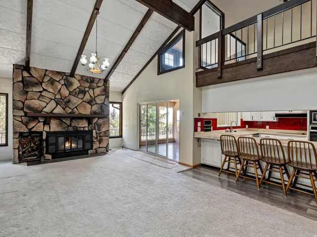 Great room featuring a prominent stone fireplace, vaulted ceiling with exposed wood beams, and an open loft overlooking the space