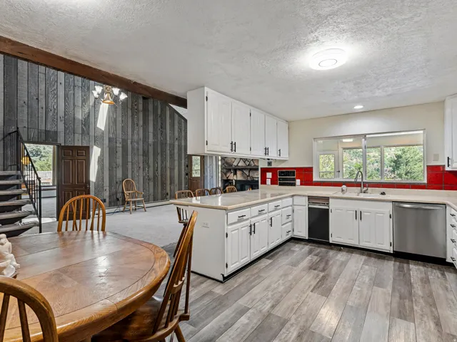 Open-concept kitchen and living area featuring wood-finish flooring, white cabinetry, and a red tile backsplash