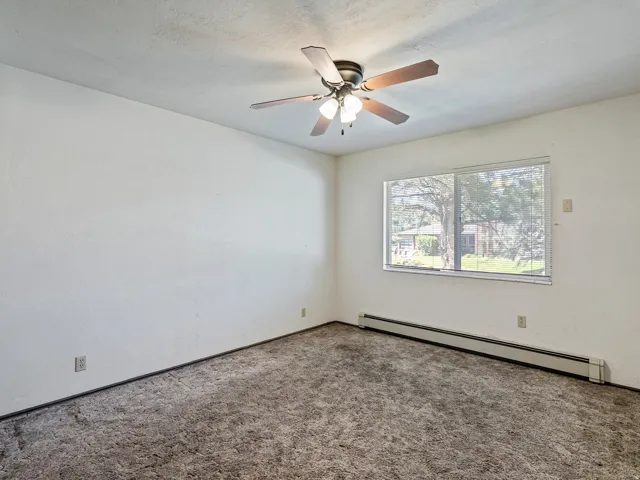 Carpeted room featuring a ceiling fan with light fixture, baseboard heating, a large window with blinds, and white textured walls