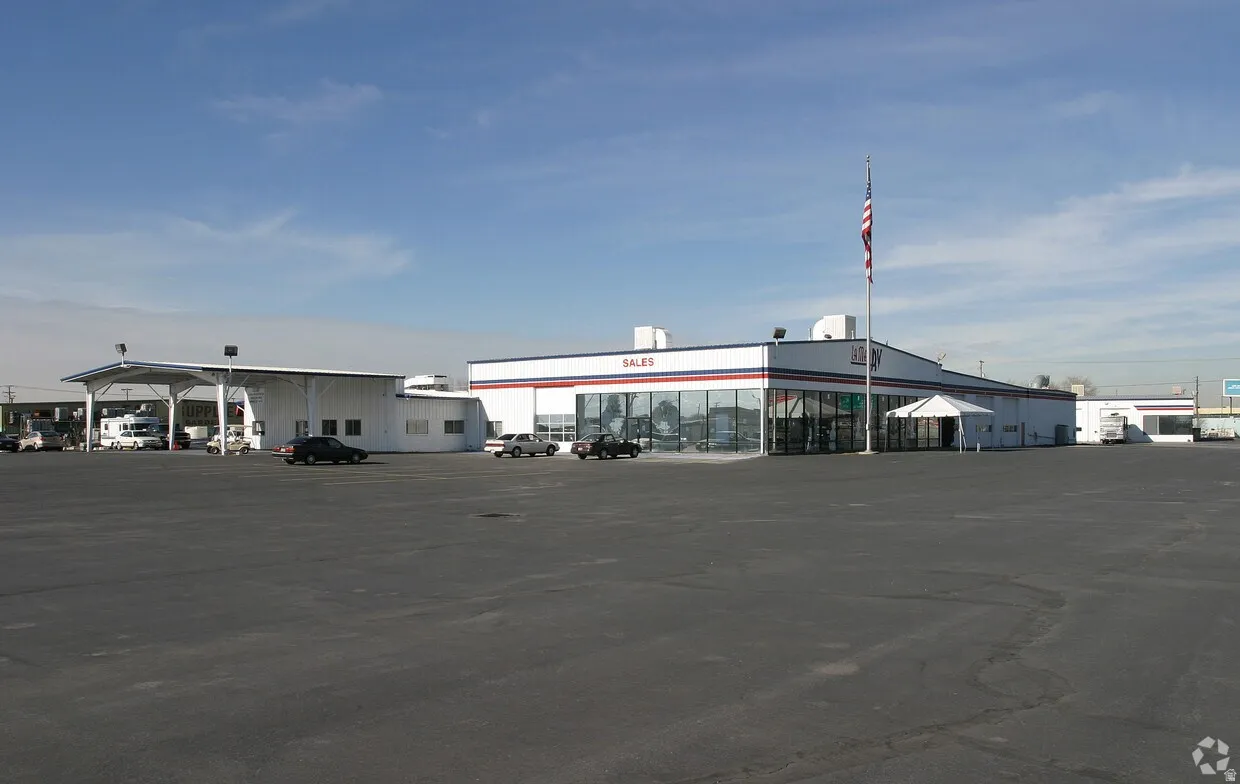 Large commercial building featuring a prominent sales showroom with expansive window displays, a covered service bay area, and a substantial paved parking lot