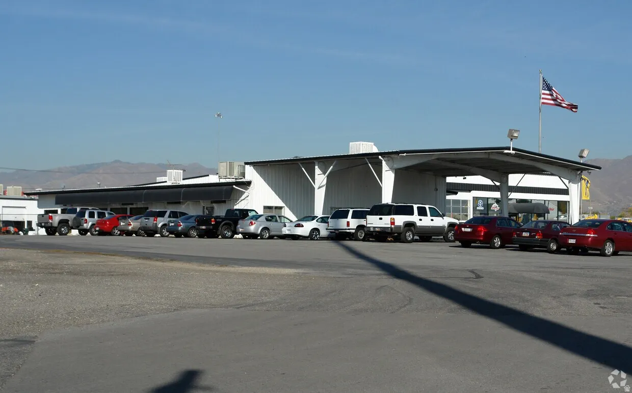 Commercial building featuring a white corrugated metal exterior, covered entry, and a large paved parking area
