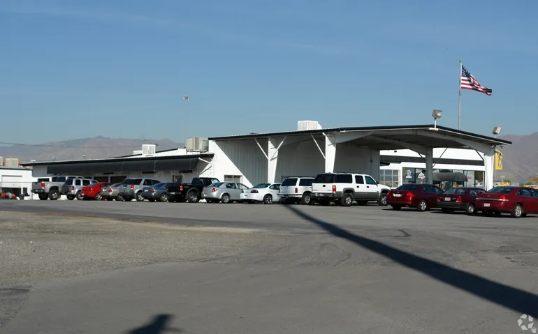 Commercial building featuring a white corrugated metal exterior, covered entry, and a large paved parking area