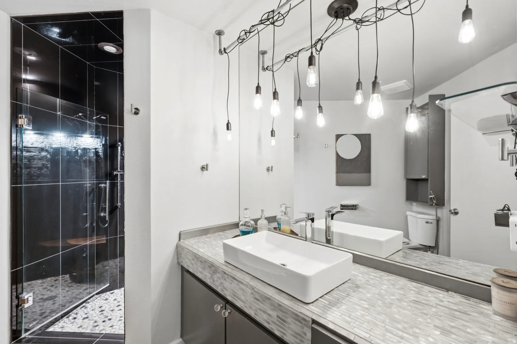 Contemporary bathroom featuring a spacious glass-enclosed shower with dark tile and pebble flooring