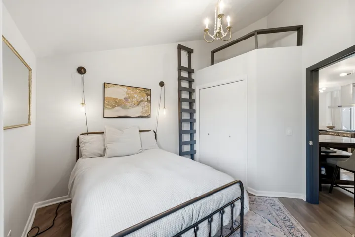 Loft bedroom featuring sloped ceilings, wood-finish flooring, and a built-in ladder providing access to an upper-level space