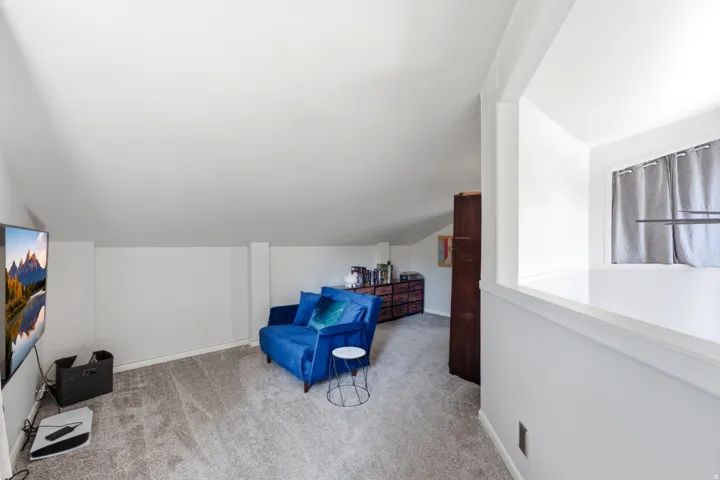 Carpeted bonus room featuring sloped ceilings, white walls, and a built-in half-wall partition