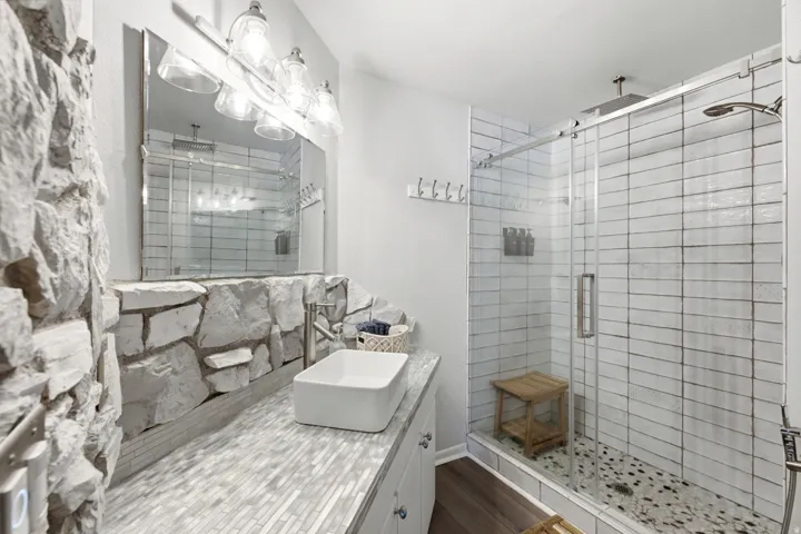 Stone accent wall with a vessel sink, mosaic tile countertop, and brushed nickel faucet