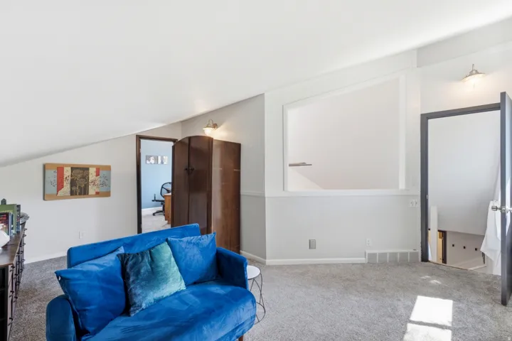 Carpeted loft area featuring a sloped ceiling, built-in wall niche, and an open doorway