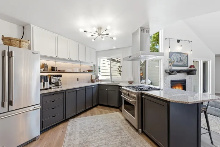 Contemporary kitchen featuring a stainless steel refrigerator, stainless steel range with hood, granite countertops, two-tone cabinetry with upper white and lower charcoal finishes, and wood-finish flooring