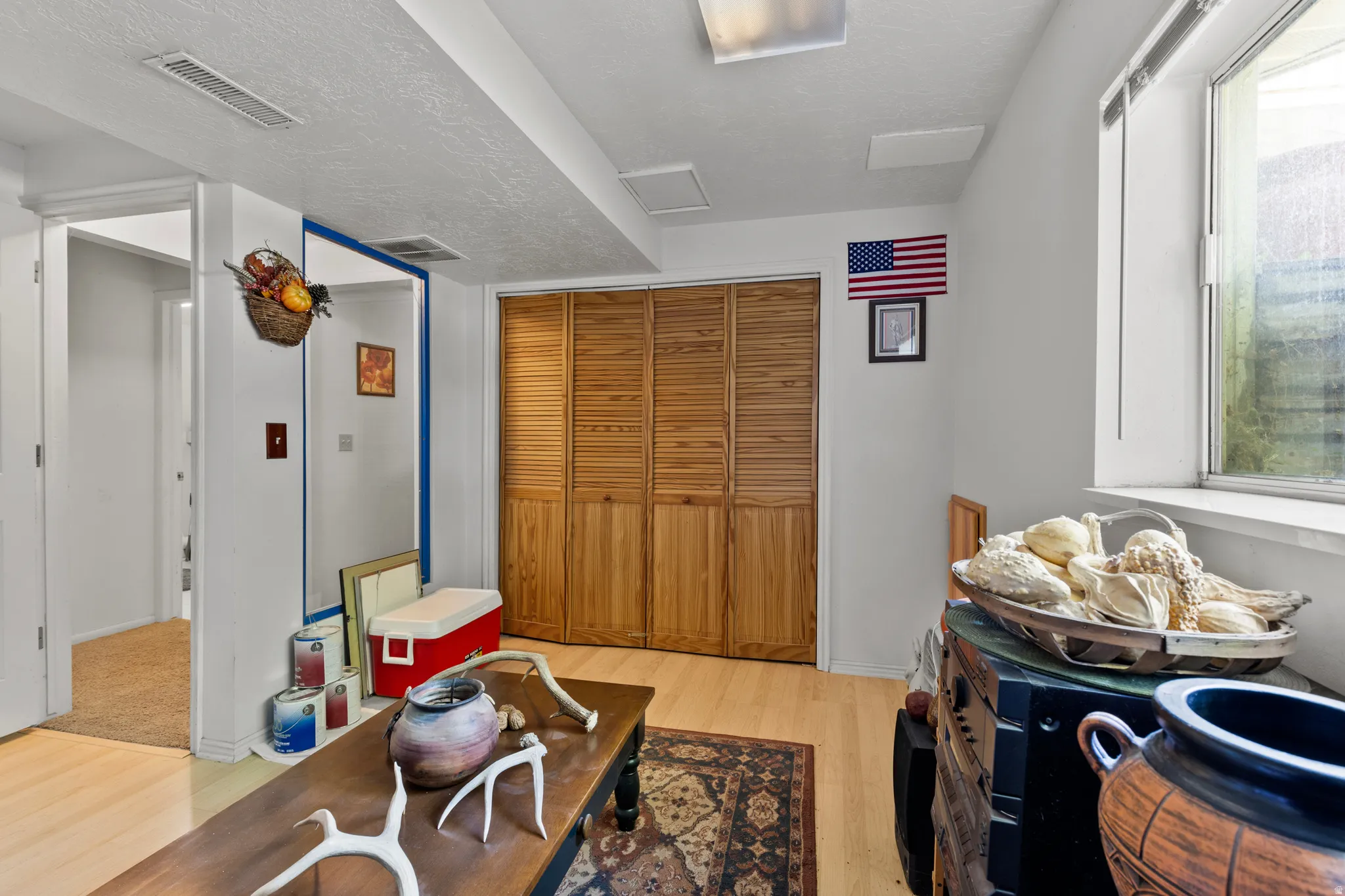 Room featuring light wood-finish flooring, a full-height bi-fold closet with wood louvered doors, and white walls