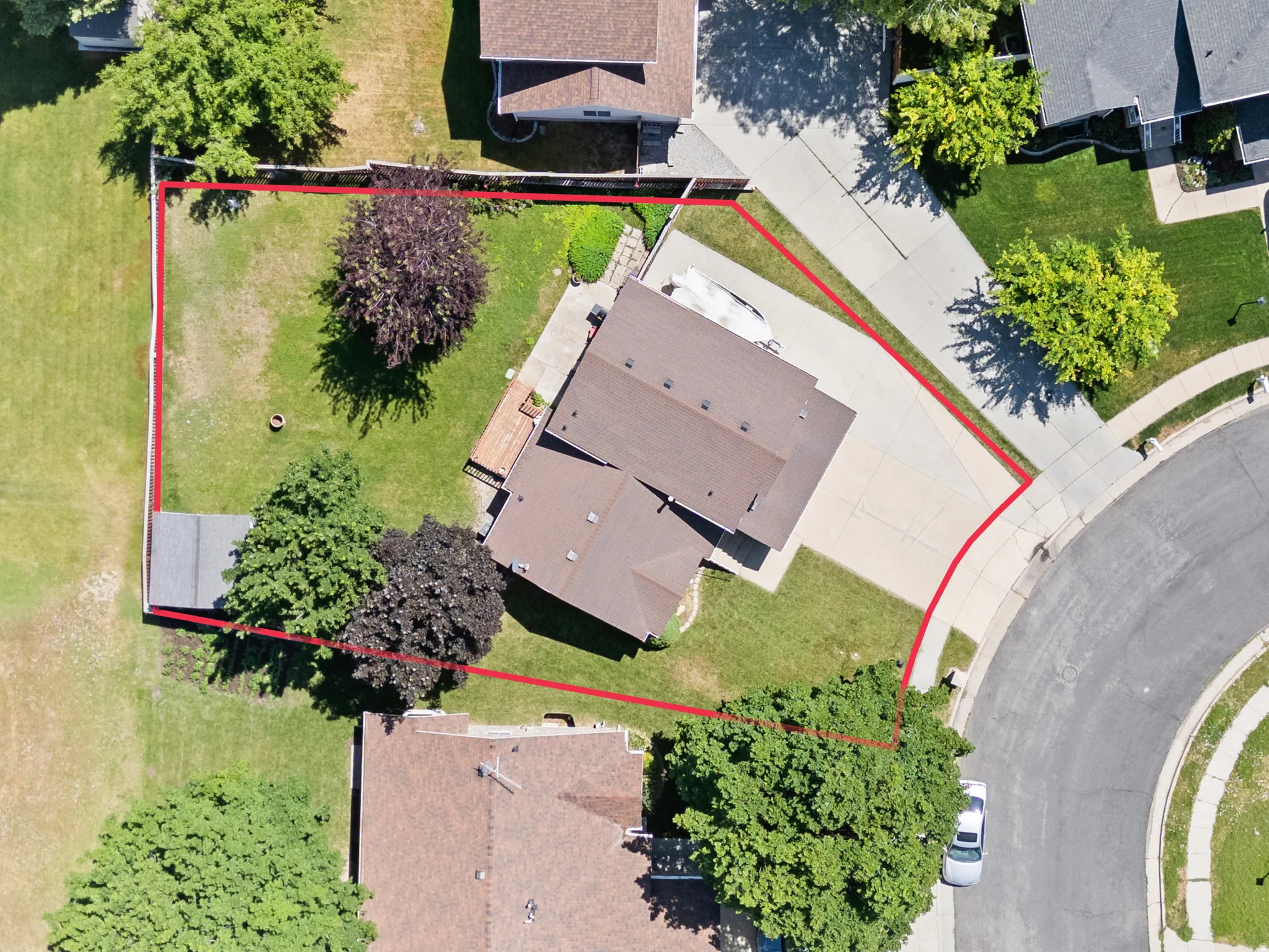 Aerial view showcasing the property's perimeter, a large paved driveway, and a spacious backyard with mature trees