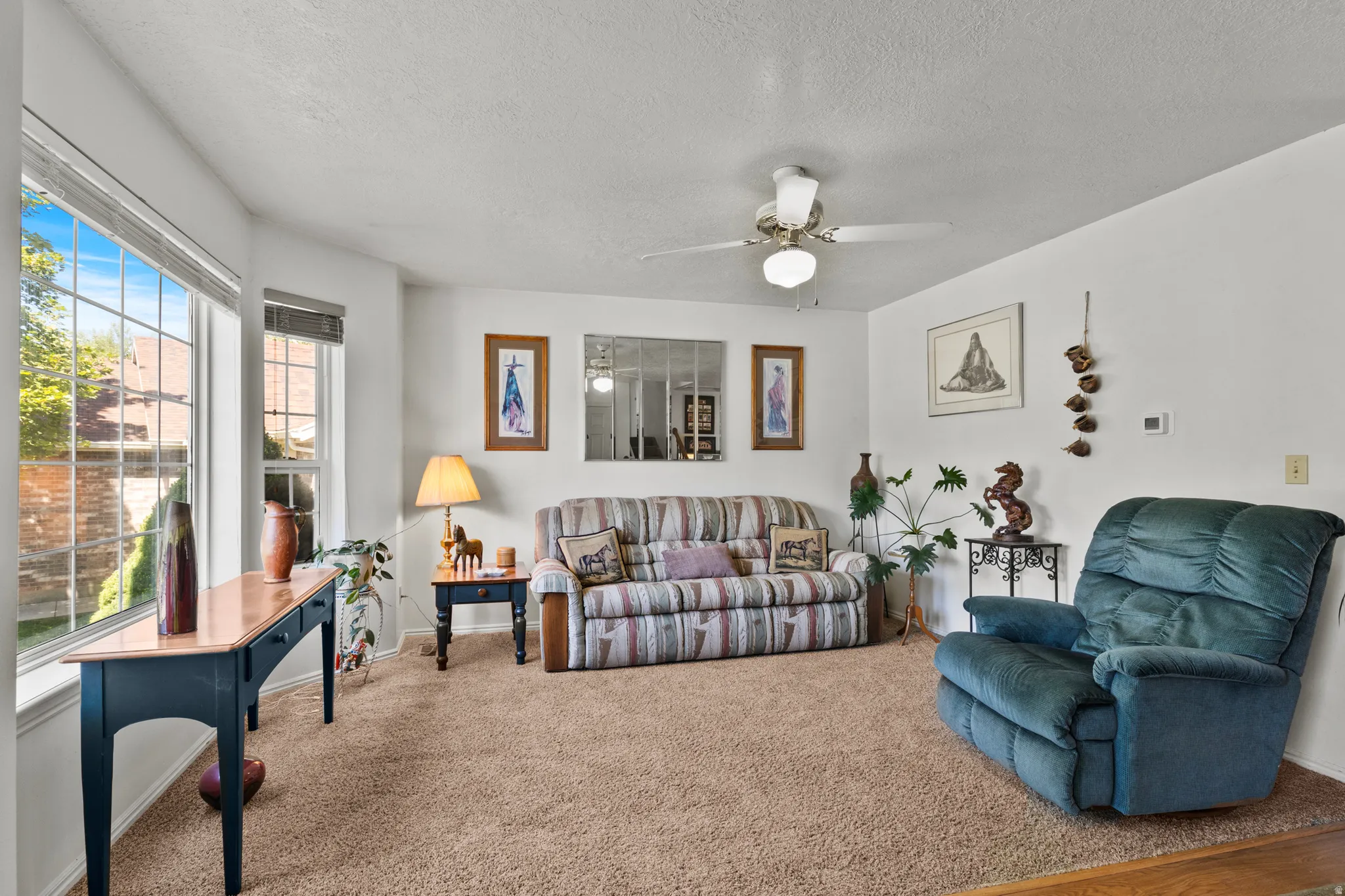 Bright living space featuring a bay window, neutral carpeting, a ceiling fan, and white walls