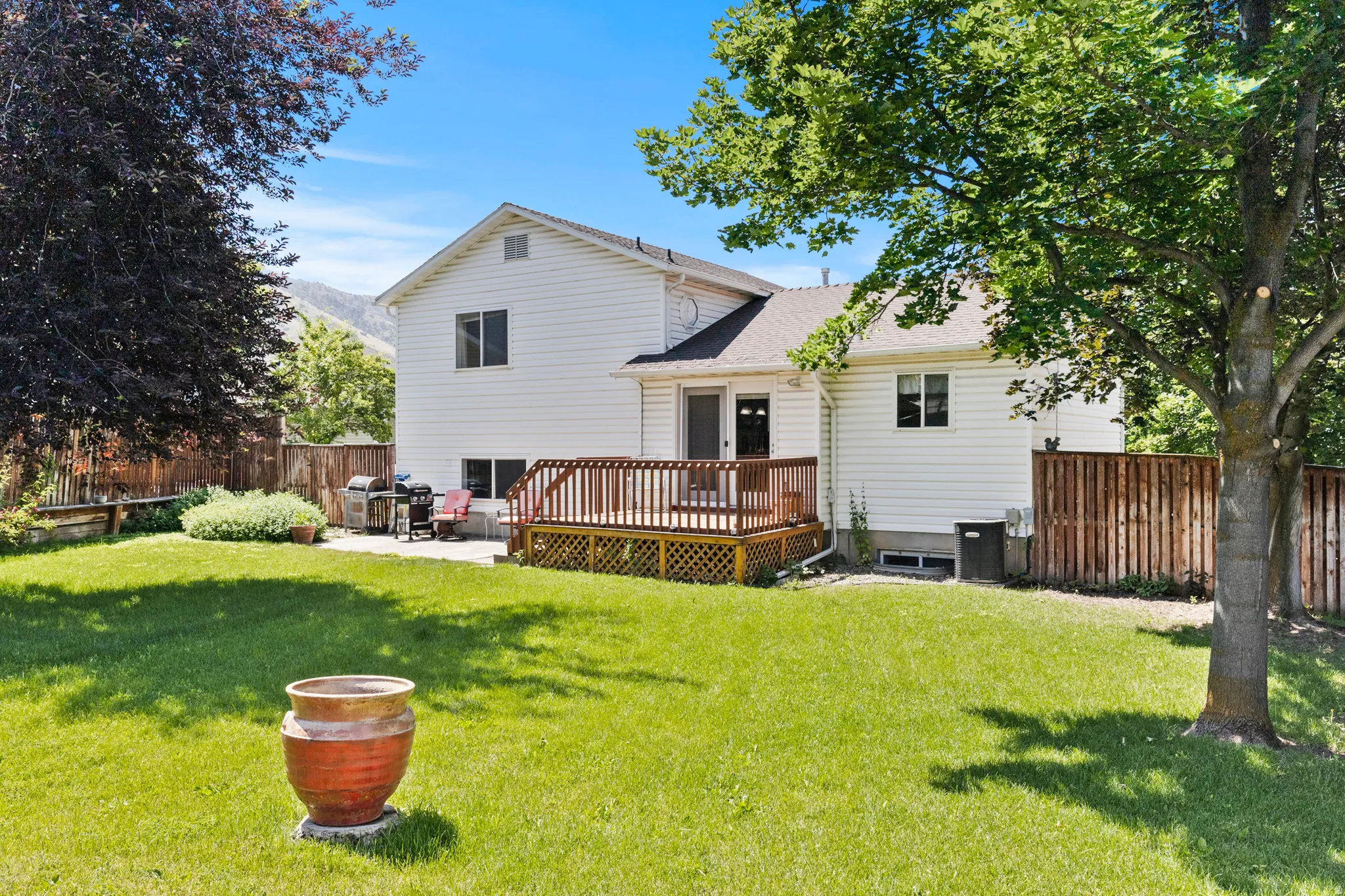 Expansive backyard featuring a wood deck, concrete patio, and mature trees