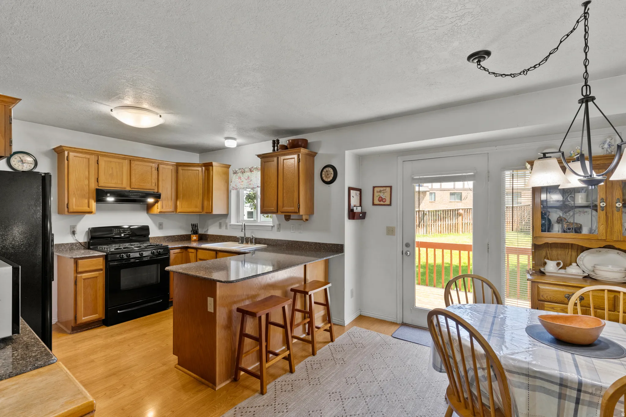 Kitchen featuring wood cabinetry, black appliances, a central island with seating, wood-finish flooring, and direct access to a rear deck