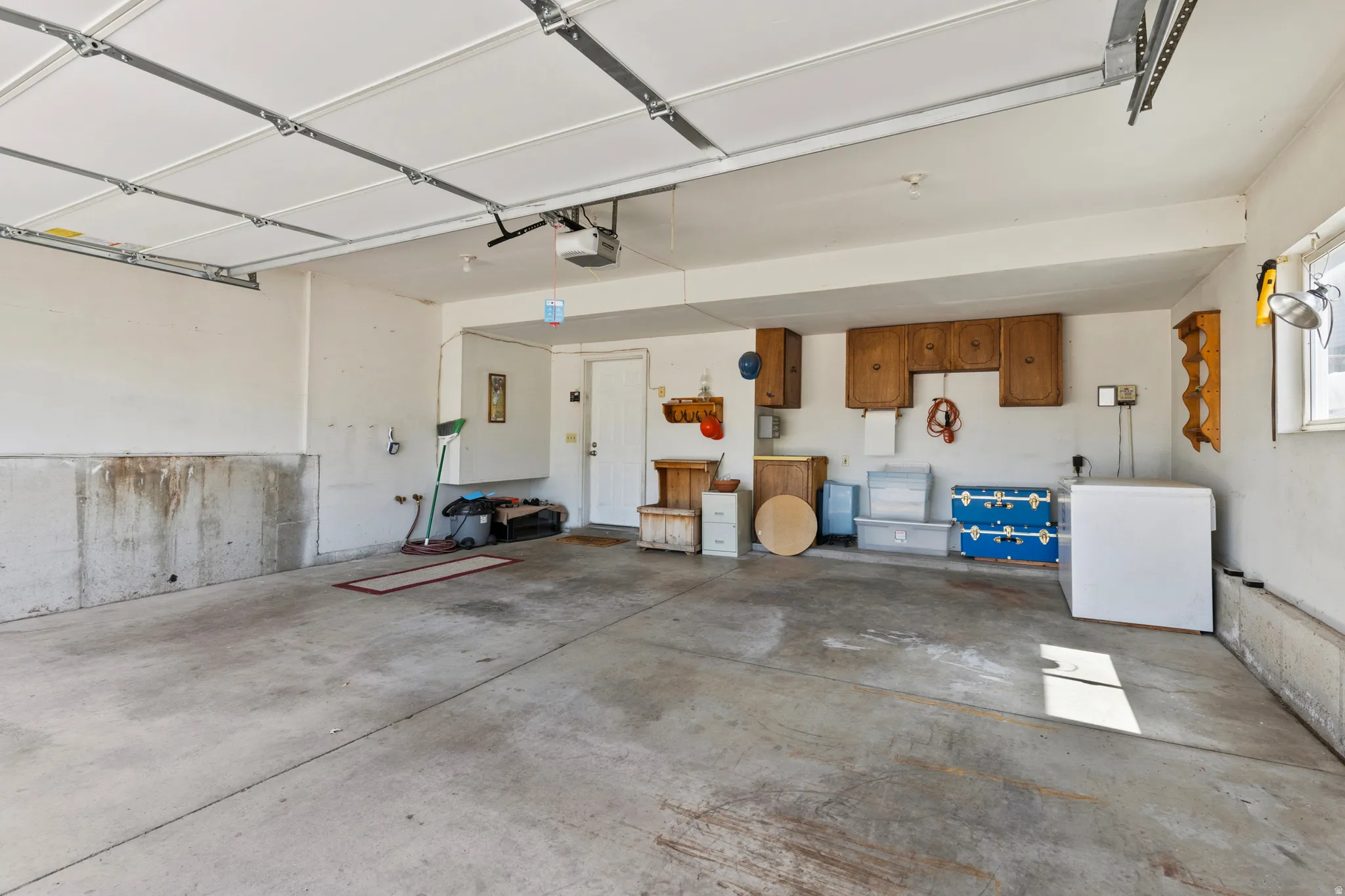 Spacious garage featuring a concrete floor, overhead garage door with opener, built-in wooden cabinetry, and a window providing natural light