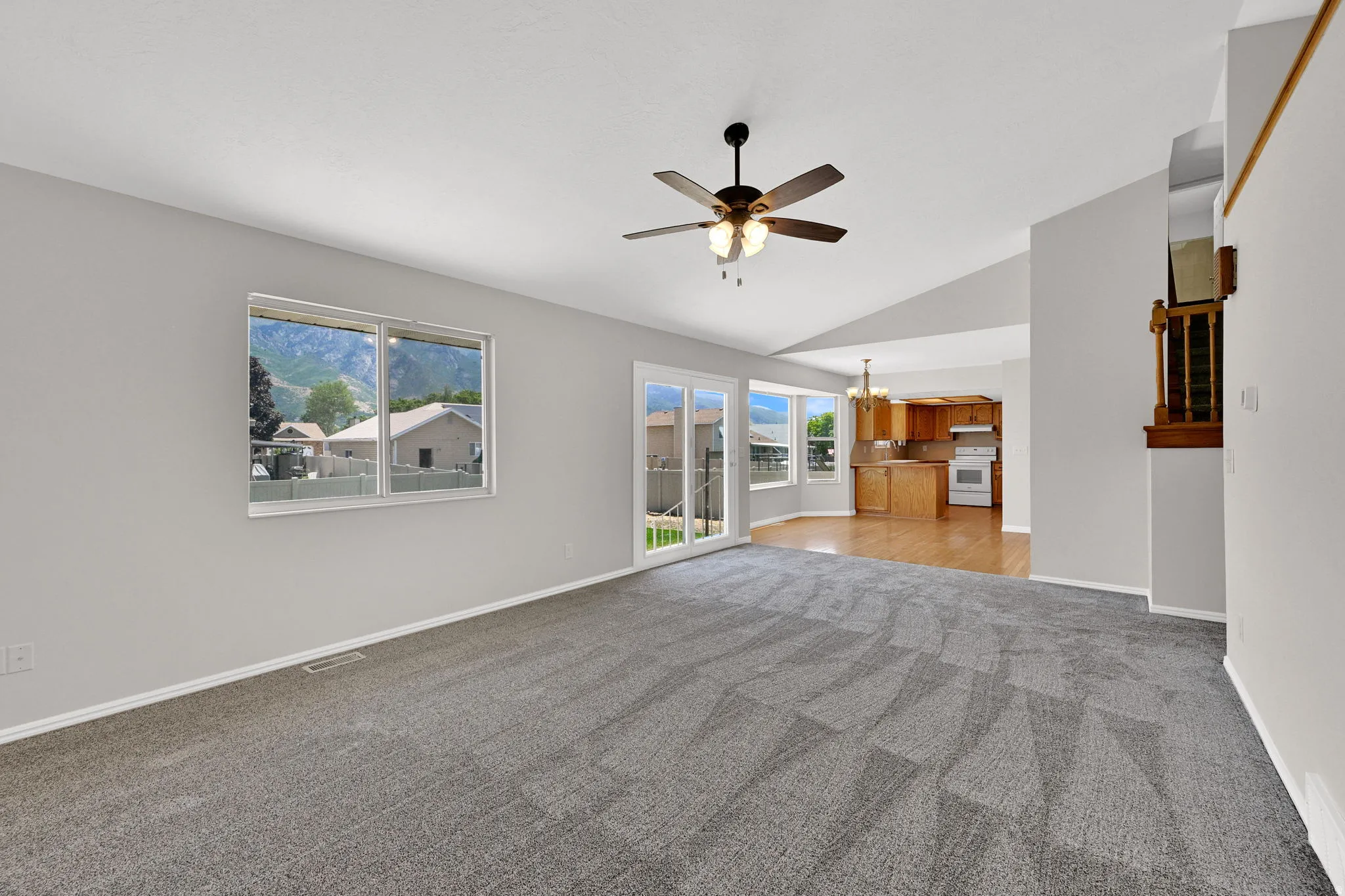 Spacious living area featuring neutral carpeting, a ceiling fan with integrated lighting, and vaulted ceilings