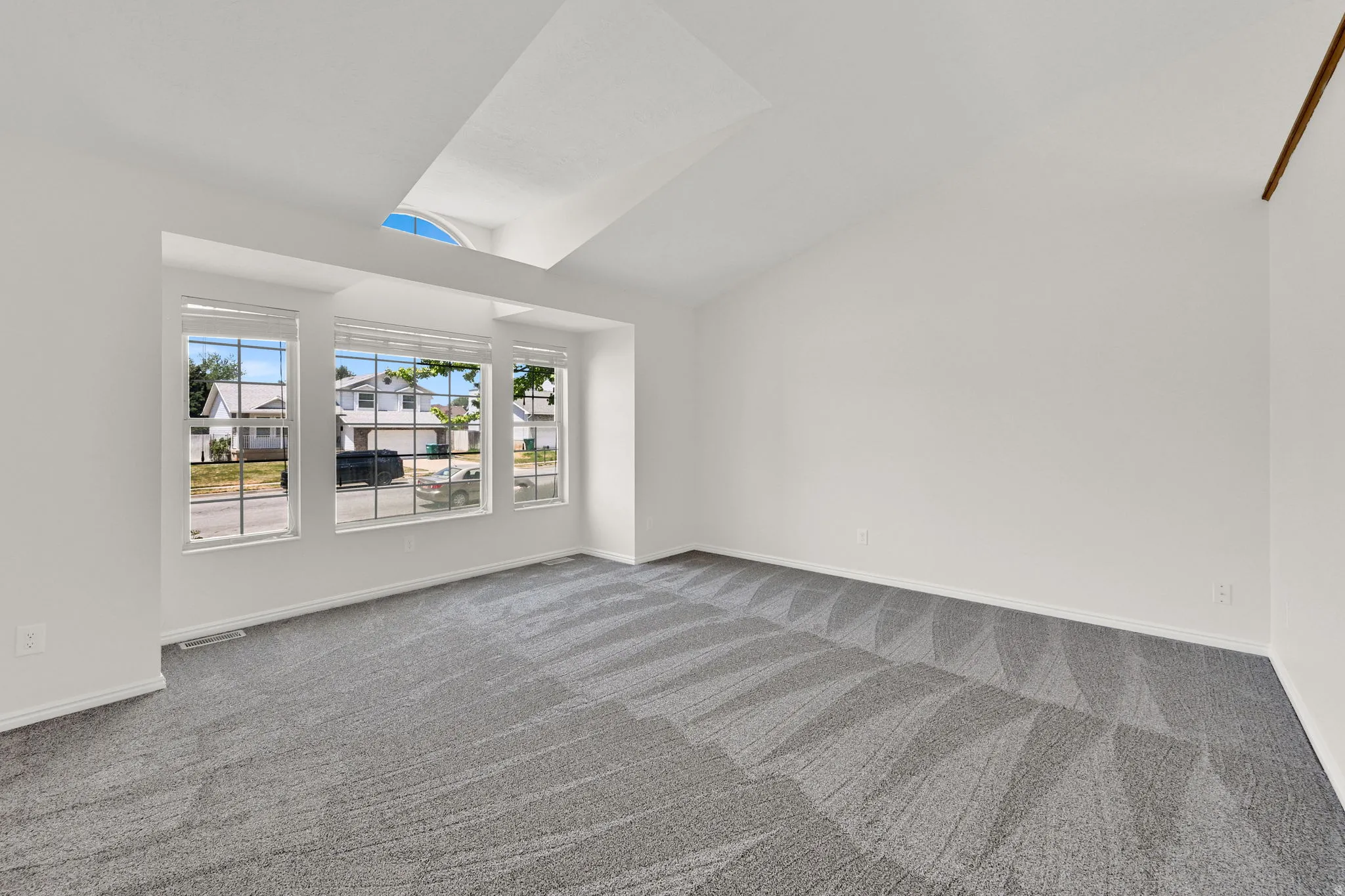 Spacious room featuring vaulted ceilings, a large bay window, an arched window detail, and neutral carpet flooring