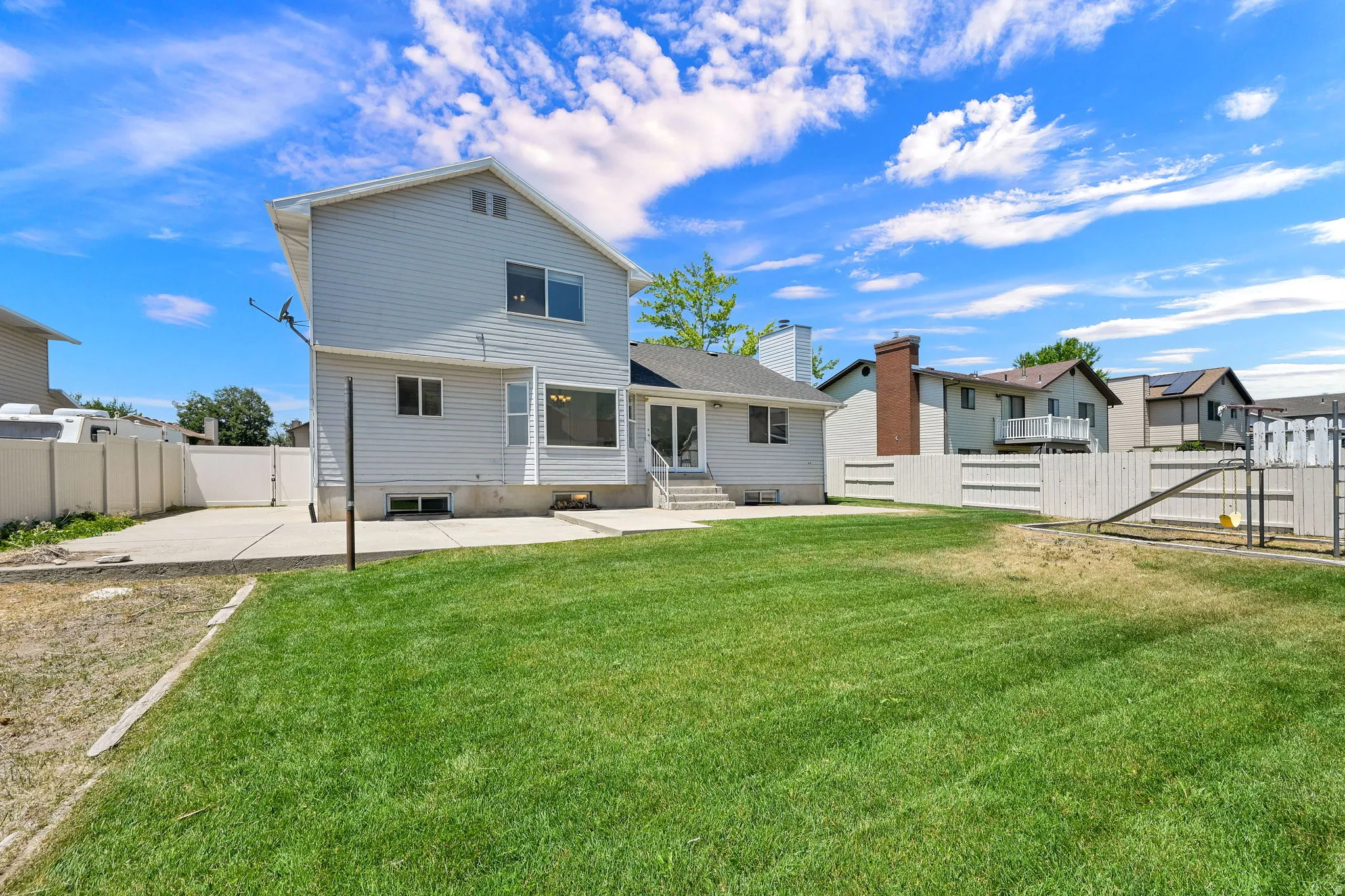 Spacious rear yard featuring an expansive lawn, concrete patio, and a privacy fence