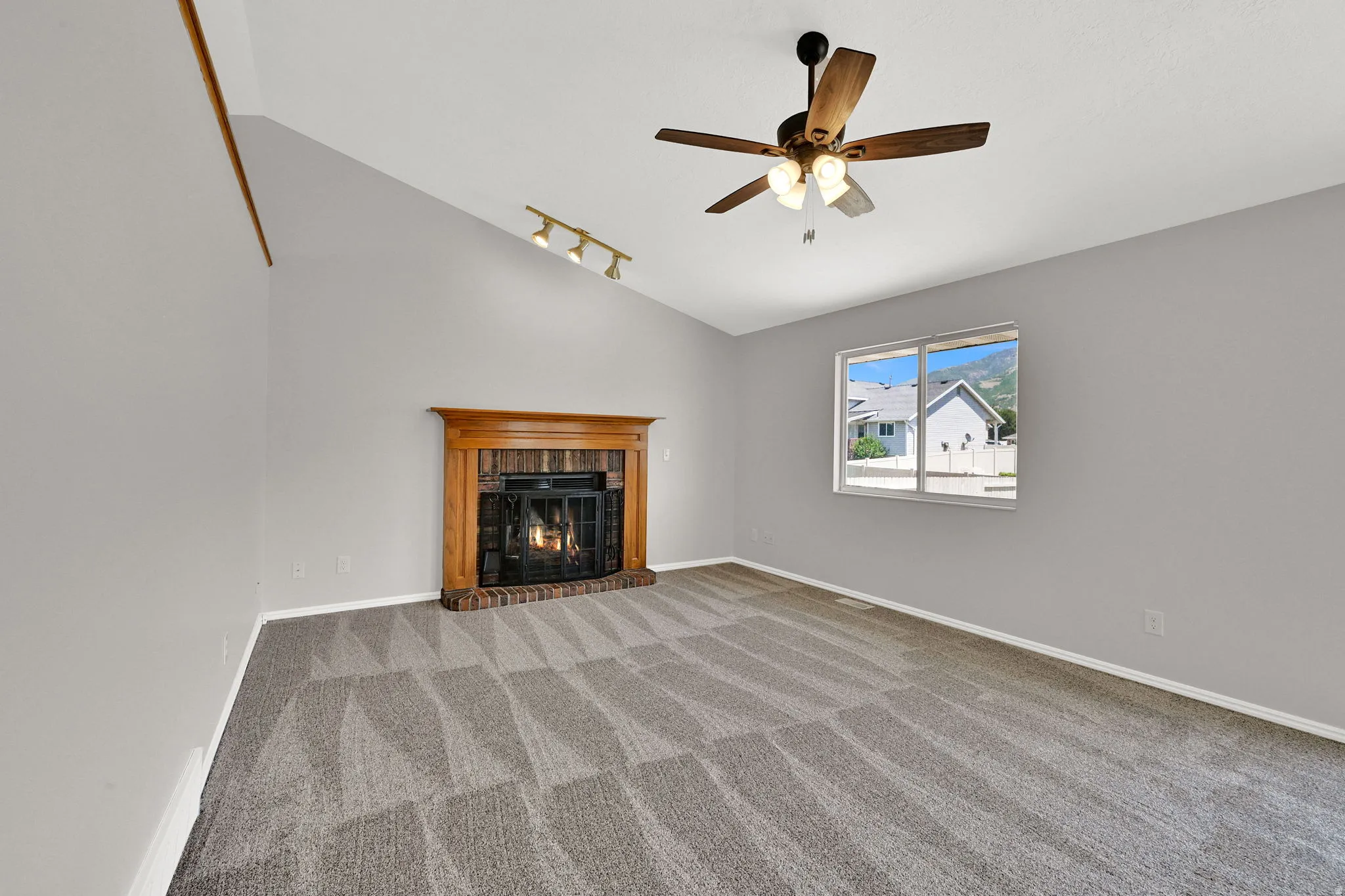 Spacious room featuring vaulted ceilings, a brick fireplace with a wood mantel, and patterned carpeting