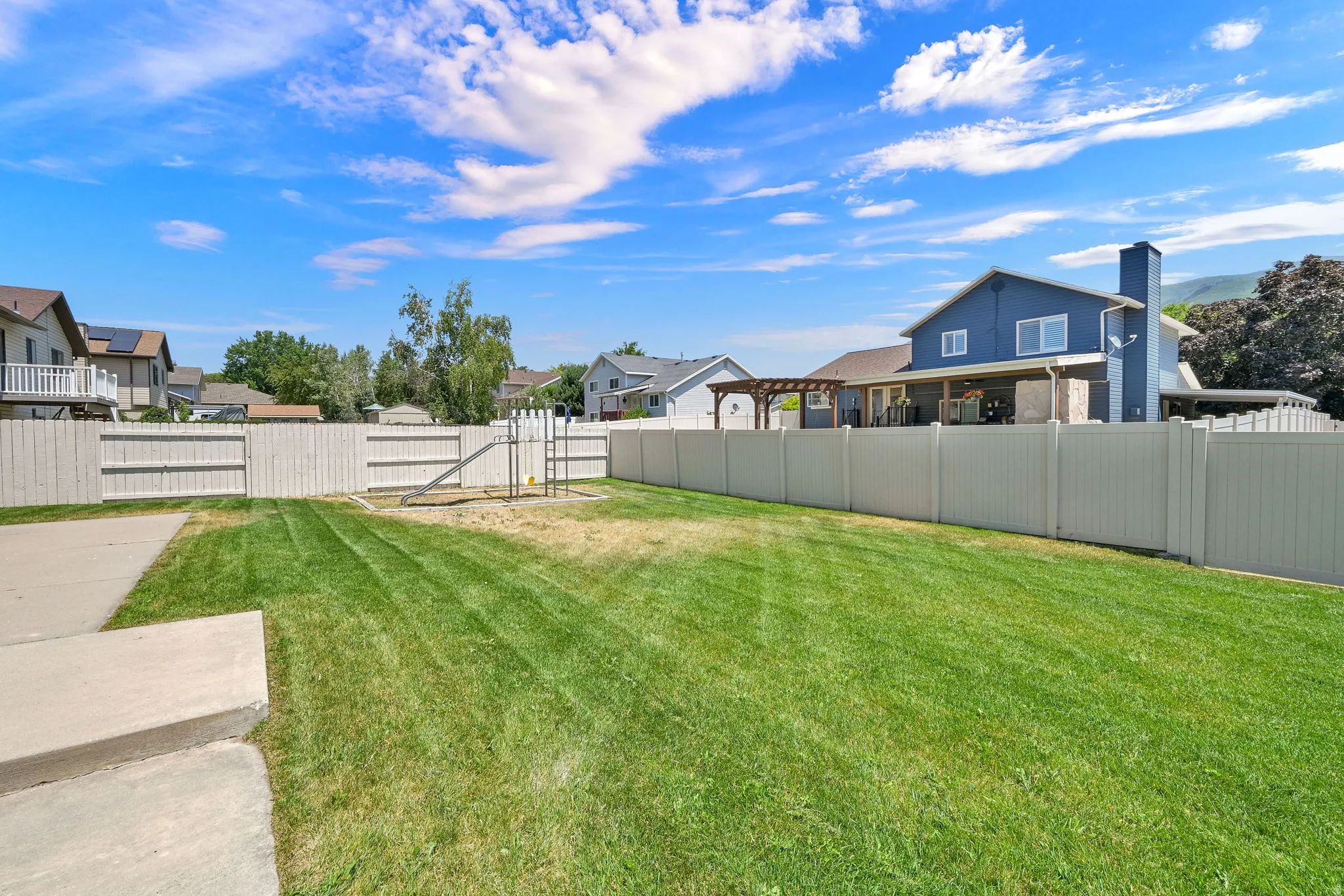 Expansive backyard featuring a manicured lawn, a concrete patio, and a privacy fence enclosing the property