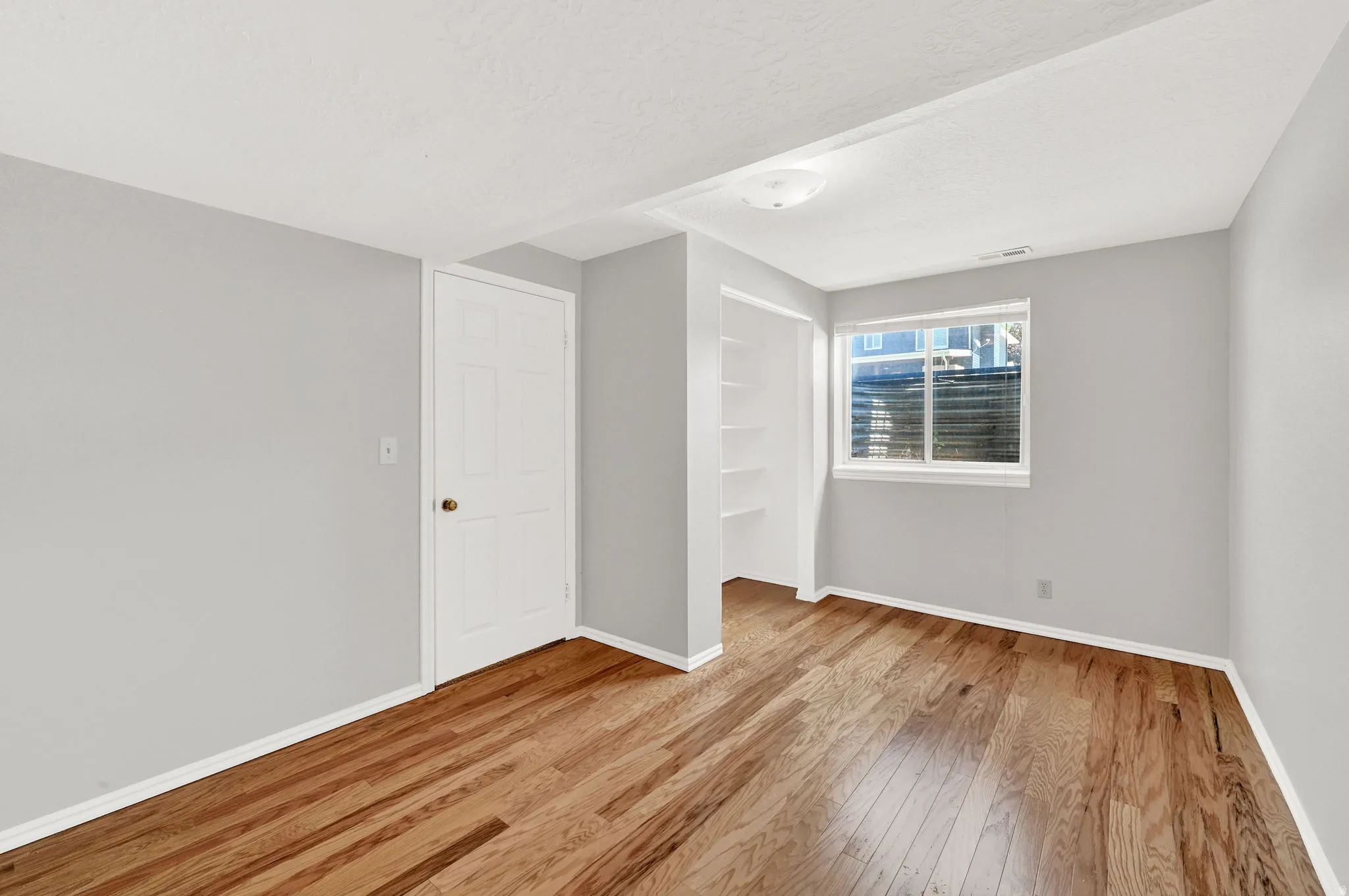 Room featuring wood-finish flooring, light grey walls, white trim, and a window