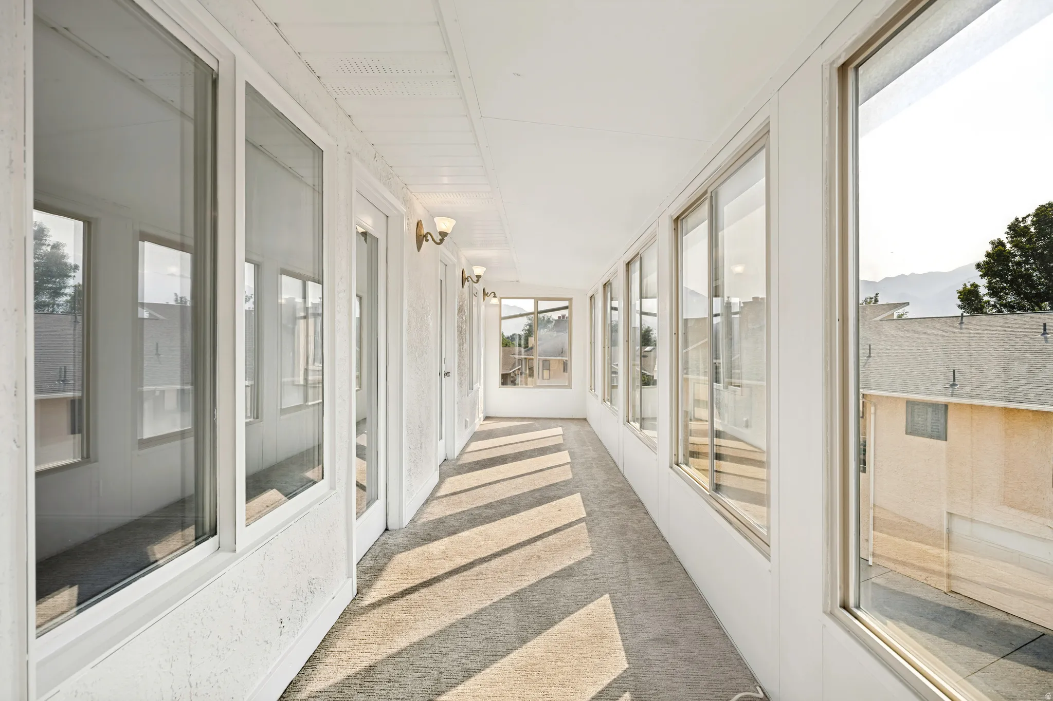 Enclosed sunroom featuring multiple large windows, wall-mounted sconces, and neutral carpeting