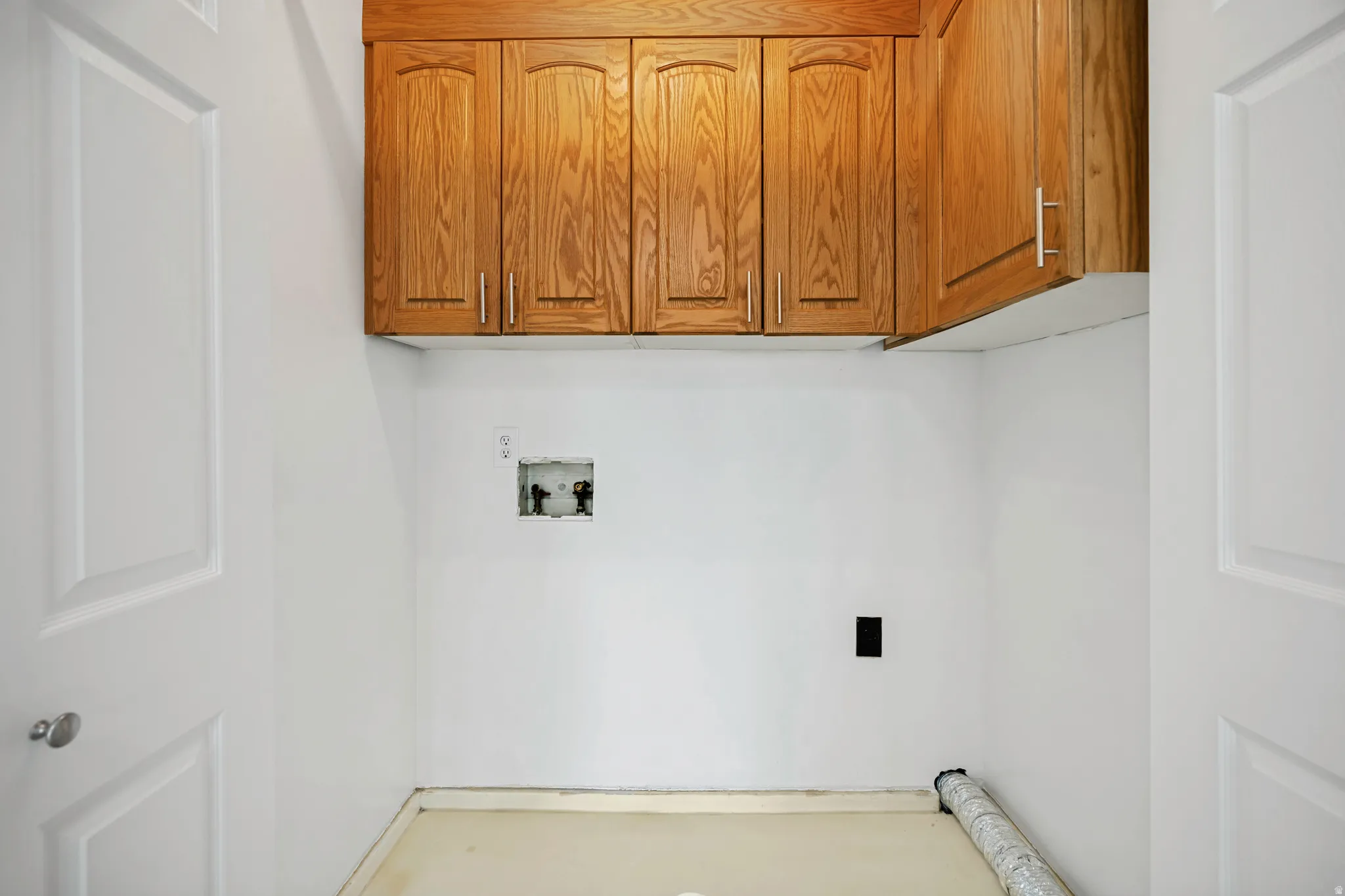 Laundry area featuring wood-finish cabinetry with silver-tone hardware, white walls, and a light-toned floor