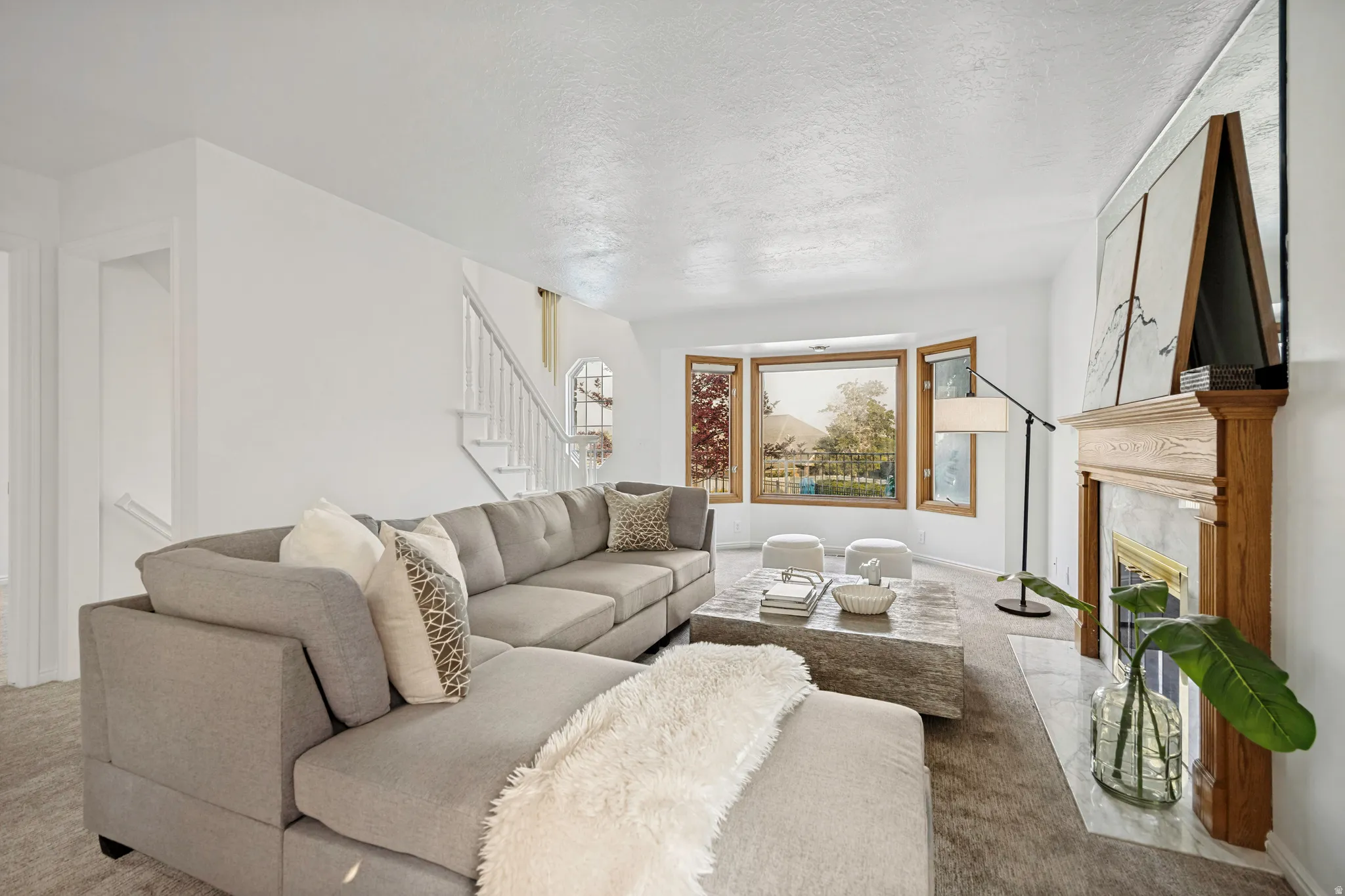 Living area featuring a bay window, a wooden mantelpiece with a tile surround, and a staircase with white balusters