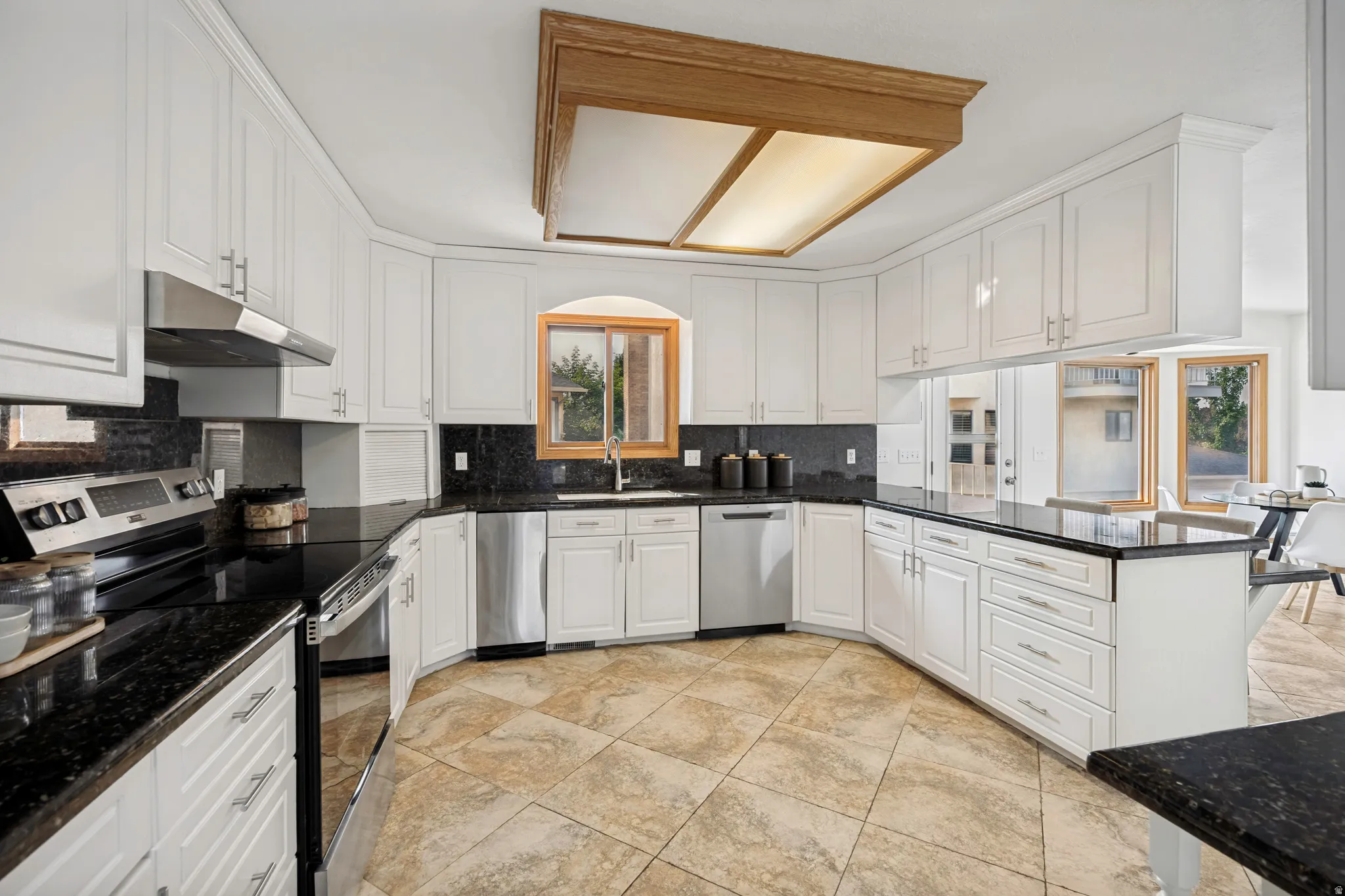 Spacious kitchen featuring extensive white cabinetry, dark stone countertops, stainless steel appliances, a built-in dishwasher, and tiled flooring