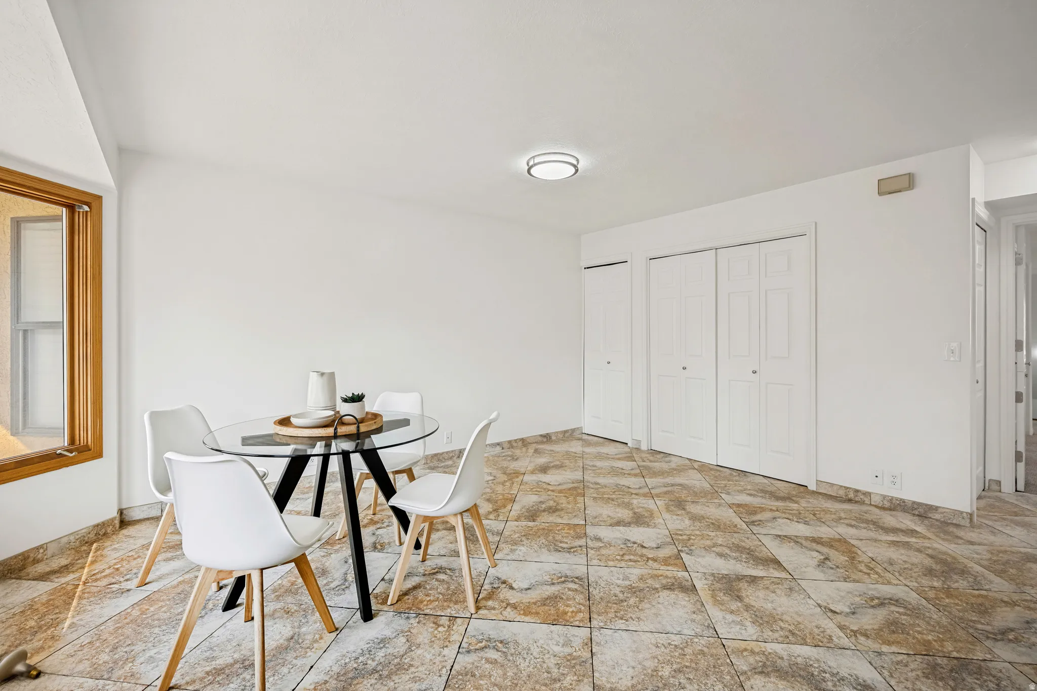Spacious room featuring neutral wall tones, a large window with natural wood trim, and durable patterned tile flooring