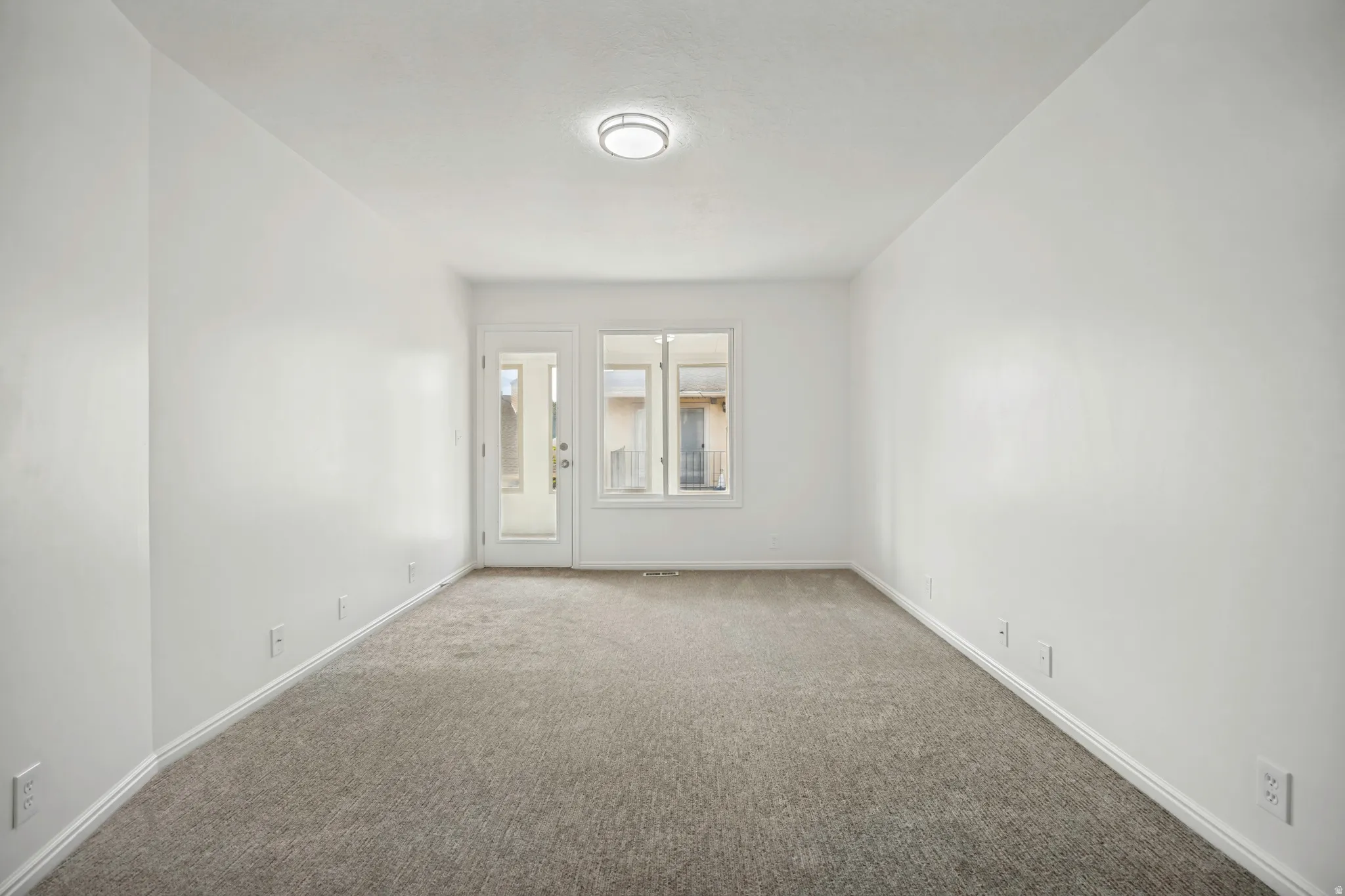 Neutral carpeted room featuring white walls and a ceiling-mounted light fixture